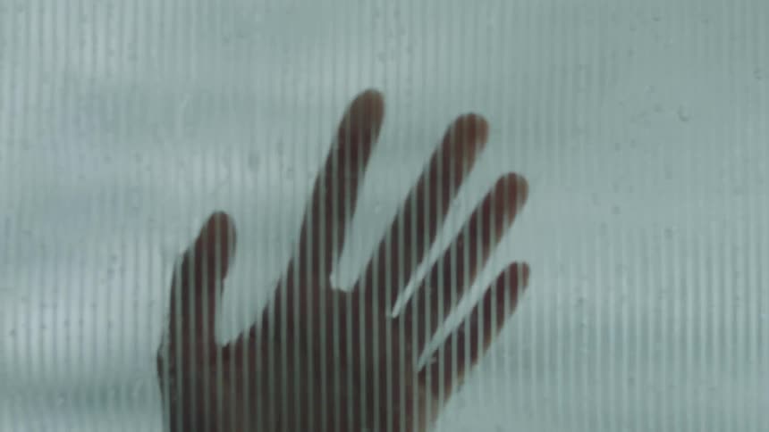 A hand slides down a rainsplattered glass pane