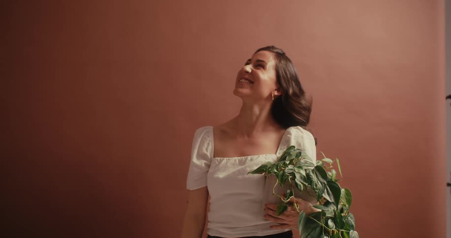 Woman in a white blouse holding a green plant and happy