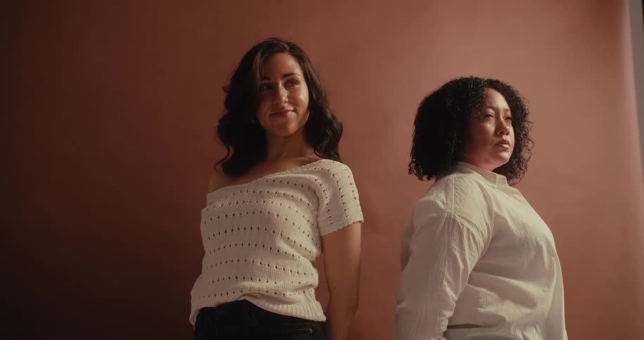 Two women are standing in front of a pink colored wall