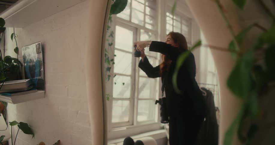 Mirror reflects a female photographer standing on a stool to take pictures of two women lying on couches in the living room