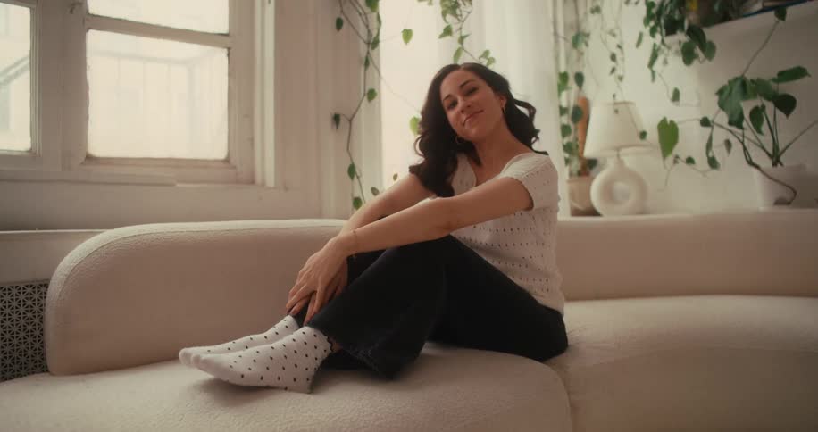 Smiling woman poses while sitting on a curved couch in her home during the daytime