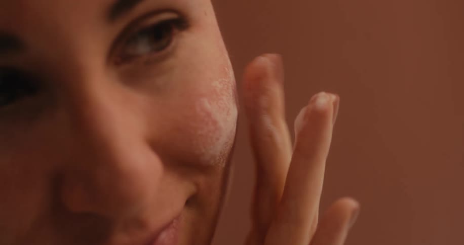 Woman smiles slightly while applying lather onto her cheek
