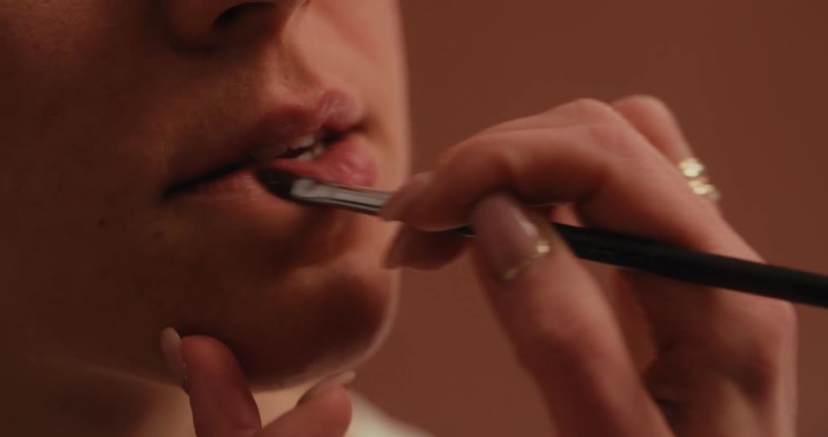 A hand with manicured nails applies makeup to a womans lips using a makeup brush