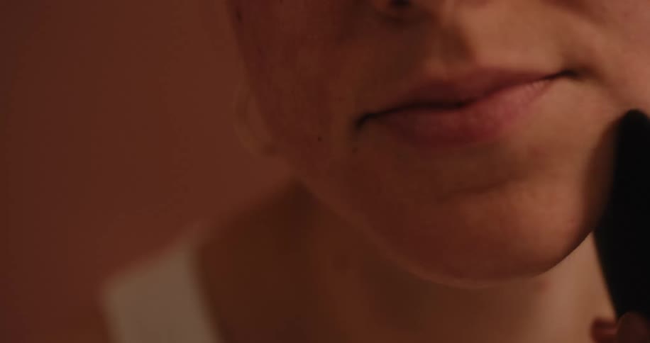 A woman uses a black gua sha tool to massage her jawbone as part of her skincare routine set against a neutral background
