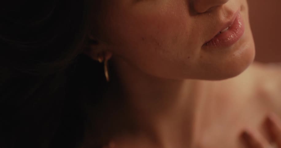 A closeup of a model wearing a white blouse with hands over the chest gold earrings and a neutral expression looking directly at the camera against a neutral background