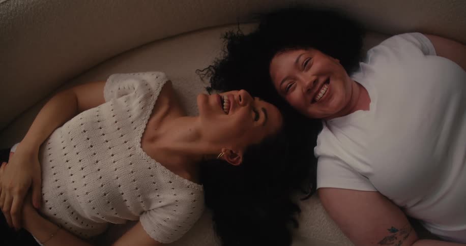 Two friends laugh while laying on the couch