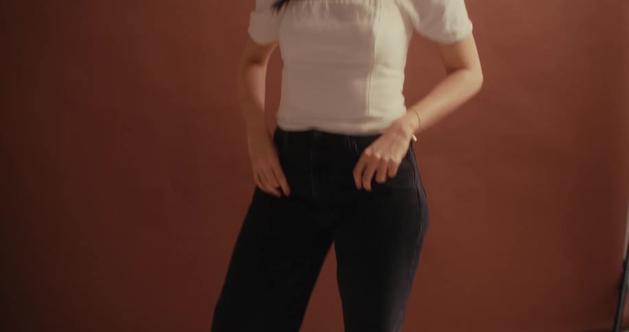 A young woman with long black hair dressed in a white dress over black trousers laughs joyfully while posing for a photoshoot
