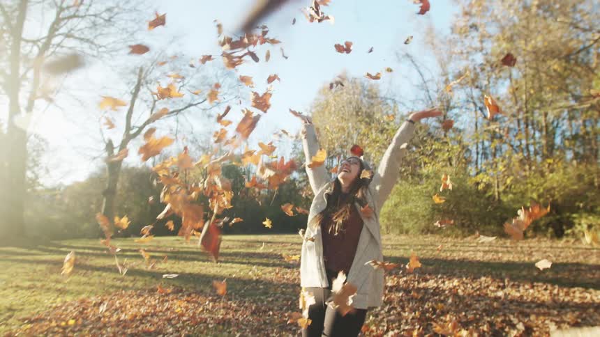Woman picking up dry leaves and throwing them up with happy facial expression