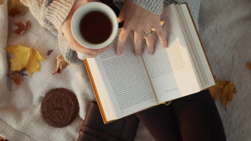 A woman is drinking coffee while reading a book