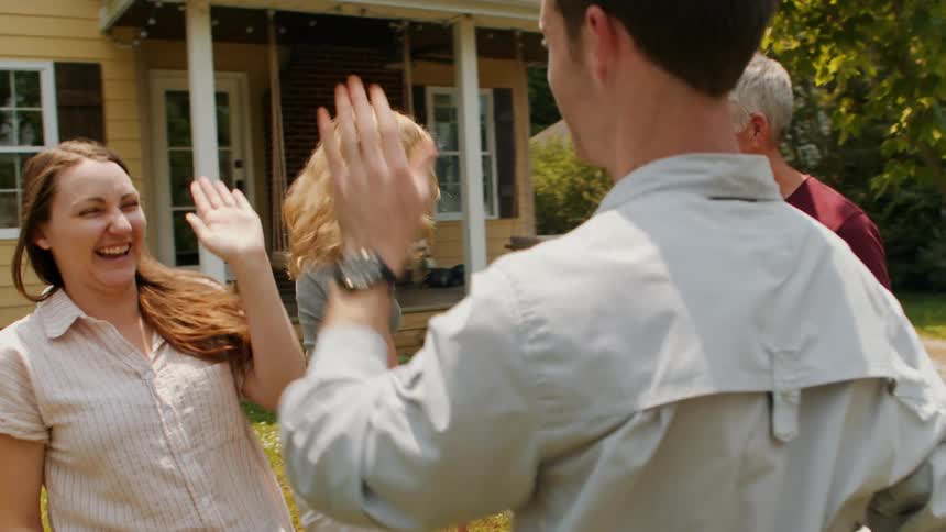 A happy family shares celebratory high fives in the front yard of their home surrounded by a cheerful atmosphere