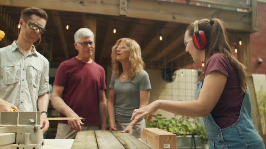 Four people outdoors two of them wearing protective gear are on a table with wooden planks