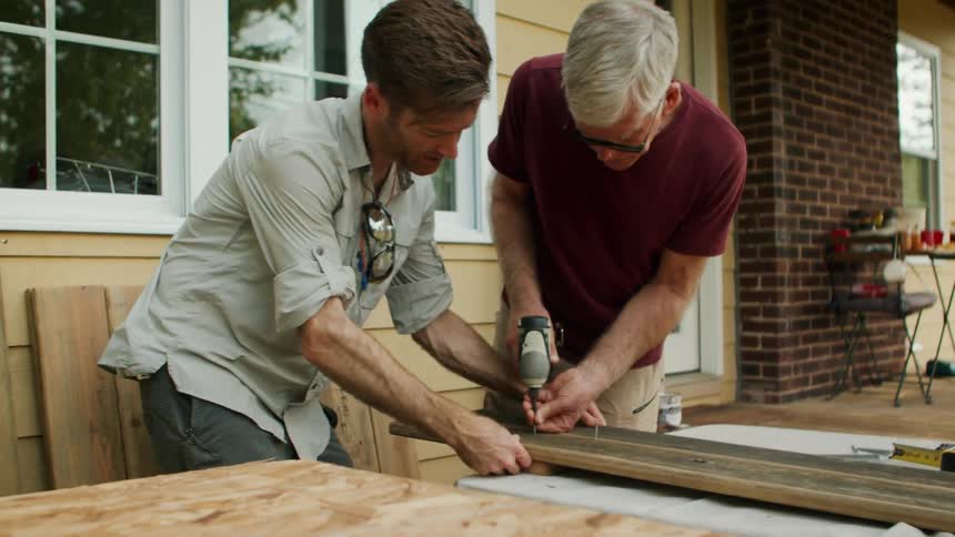 Two men screwing into a wooden slat in the backyard of a house