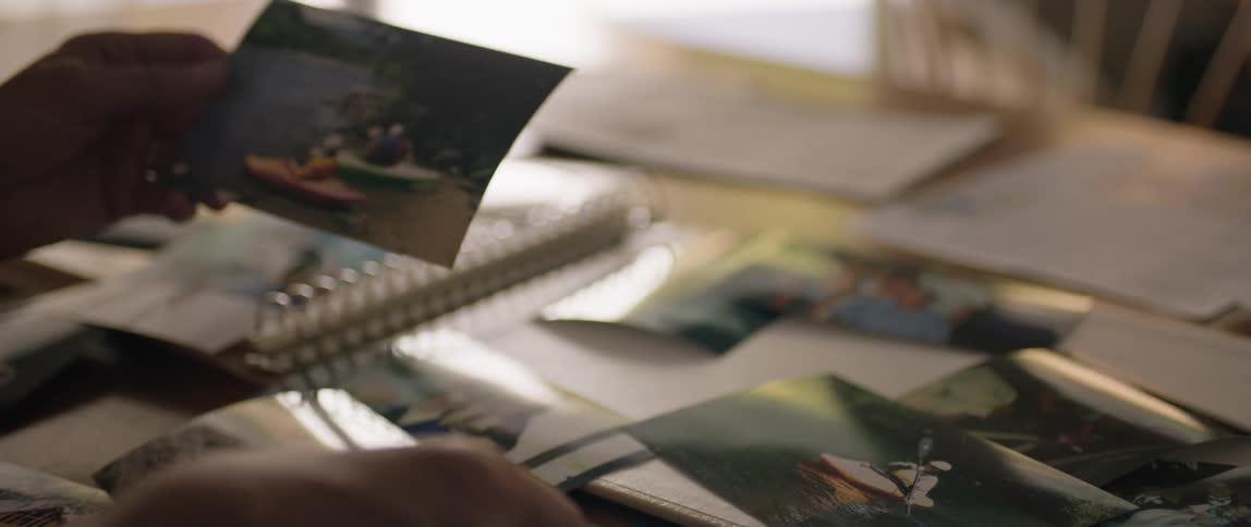 A persons arm seen sorting through a series of photographs laid out on a table indoors at midday