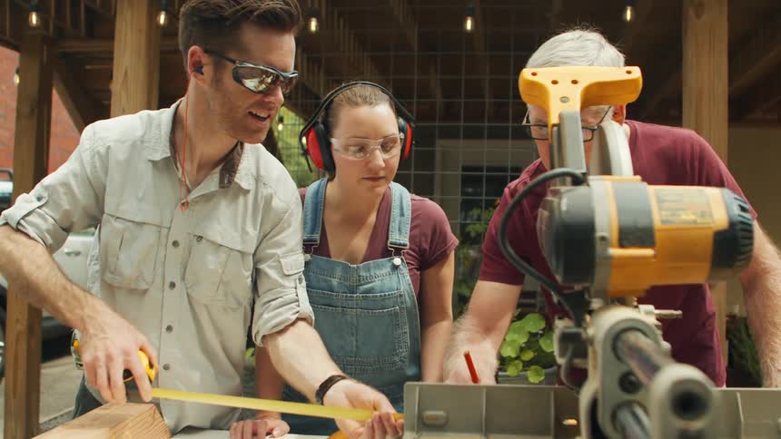 A family gathered working together on carpentry at a table with an electric saw