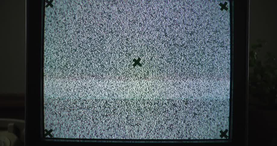 An old television displaying a blank screen with green x marks in the corners and center sits on a table next to a rotary dial telephone