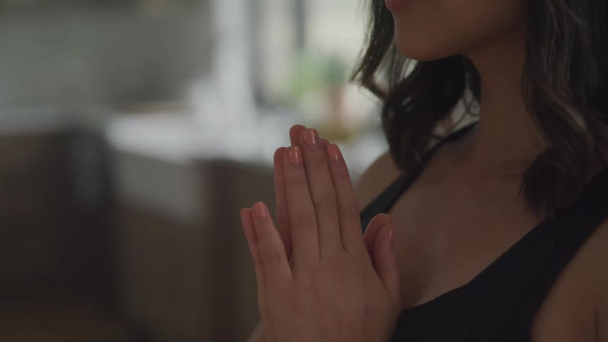 A woman stands with hands pressed together in a prayer like pose against a blurred background of a modern kitchen