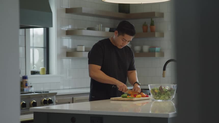 A person chops vegetables on a wooden cutting board in a modern kitchen with open shelving and white tiled walls