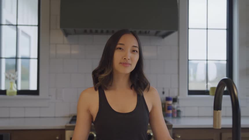 Woman in black tank top with happy facial expression while standing in kitchen