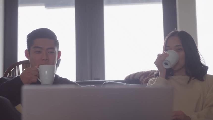 A young man and a young woman sitting having a drink and watching something on a laptop