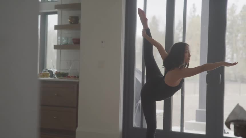 A young woman practices a ballet move at home