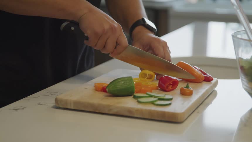 Pair of hands with knife cutting colorful bell peppers on top of chopping board