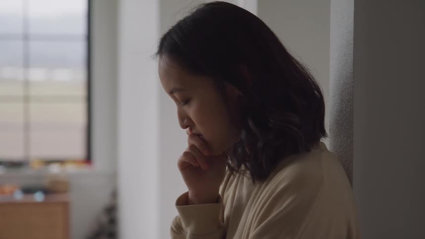A woman with shoulderlength hair reclines against a wall her hand resting on her chin in a thoughtful pose
