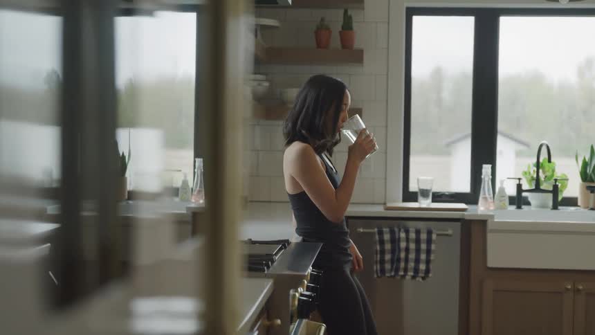 A woman is drinking water in the kitchen