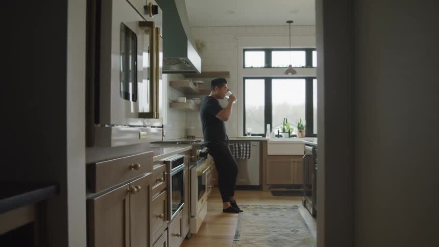 A man is drinking a glass of water in the kitchen