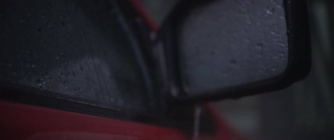 Heavy rain dripping off side rear view mirrors of a moving red vehicle