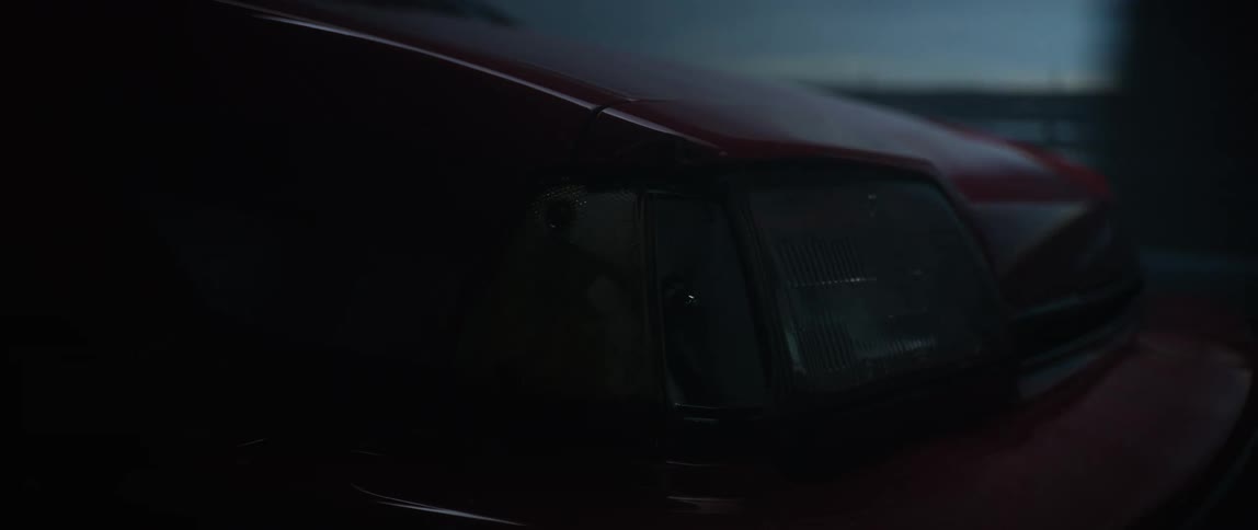 A closeup shot shows the headlight of a darkcolored car turned off while driving on a rainy bridge