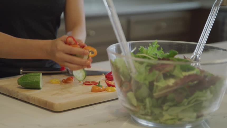 Pair of womans hands putting chopped salads into a clear bowl