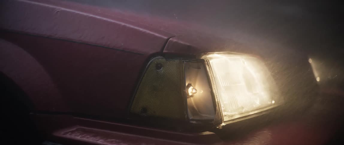 A red car sits with its headlights on in the pouring rain