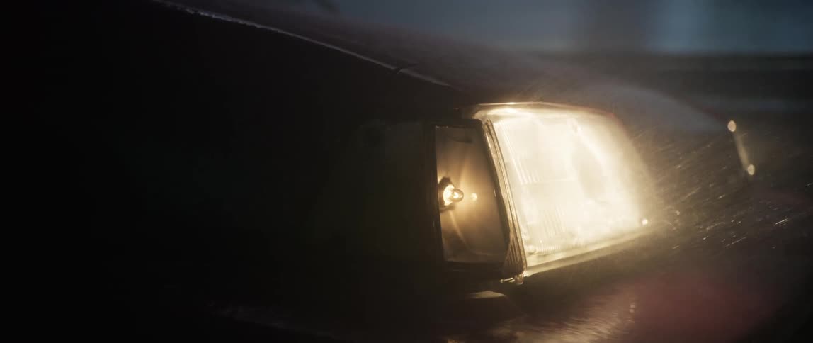A car has the headlights on as it drives in a rain storm