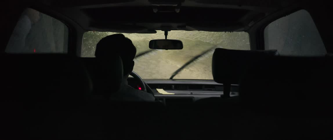 Male driver wipes the inside of his windshield while his wipers push through the rain flowing down it