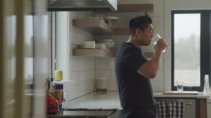 Man leaning against kitchen counter drinking water from a large glass