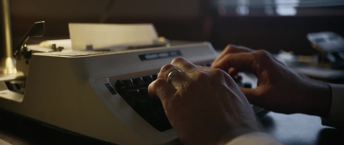 A man sits at his desk and types on his typewriter