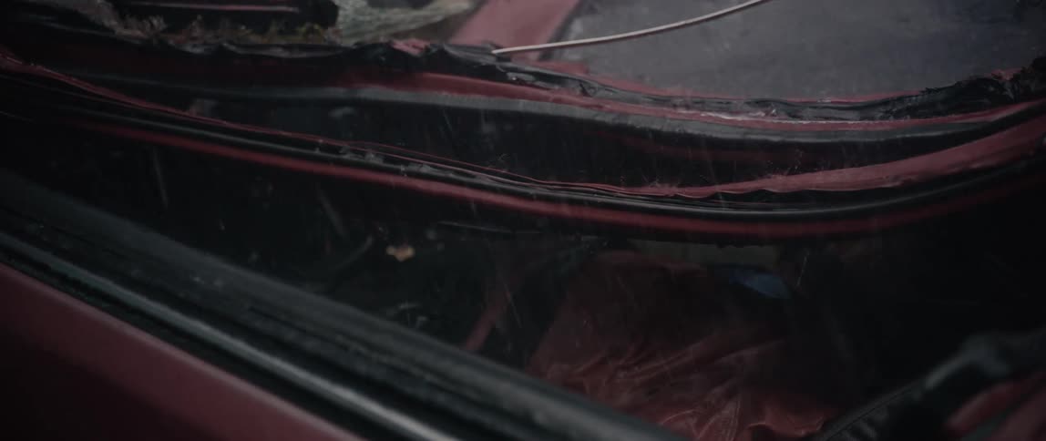 Closeup of a damaged darkred car exterior as rain patters on its surface