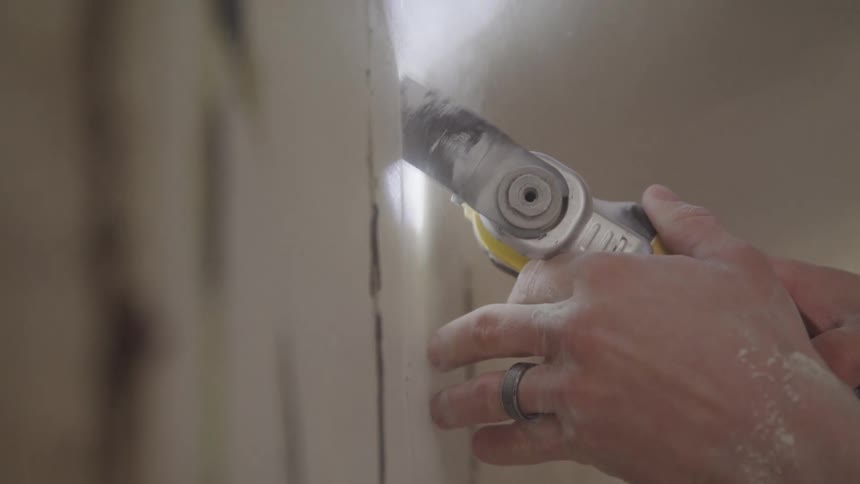 A construction worker makes cuts in the sheetrock using a cutter