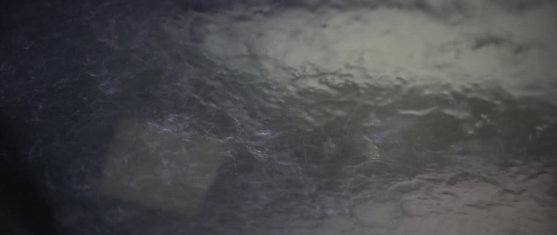 A blurry view of a road surrounded by a dense forest seen through a raincovered windshield with wipers in motion
