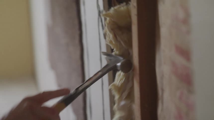 A construction worker is removing nails from a stud using a crow bar and a hammer