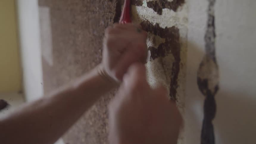 Pair of hands with a tool removing a brown crust from a wall