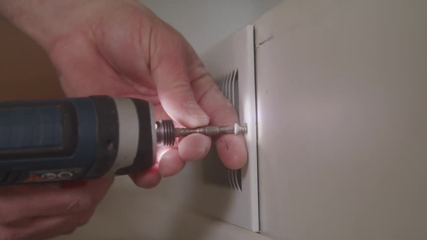 Person removing screws with a power drill from a floor vent on the wall