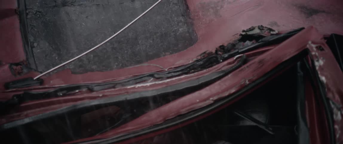 A red car has been smashed flat and it sits in the rain