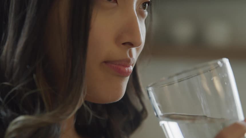 A woman drinks water from a glass and then smiles