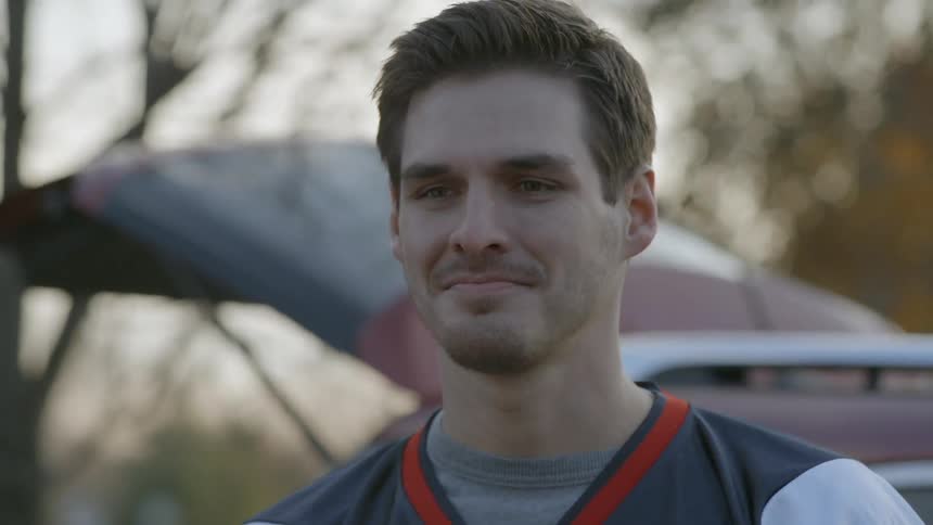 Smiling man throws a football next to a vehicle outside