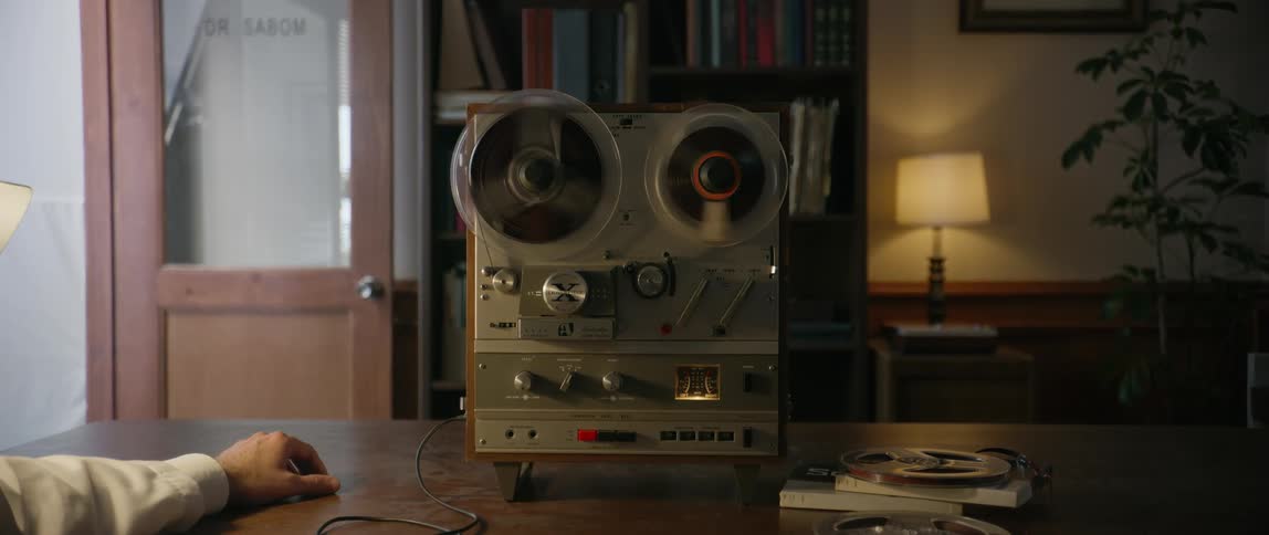 A man sitting at a table wearing headphones connected to an old radio