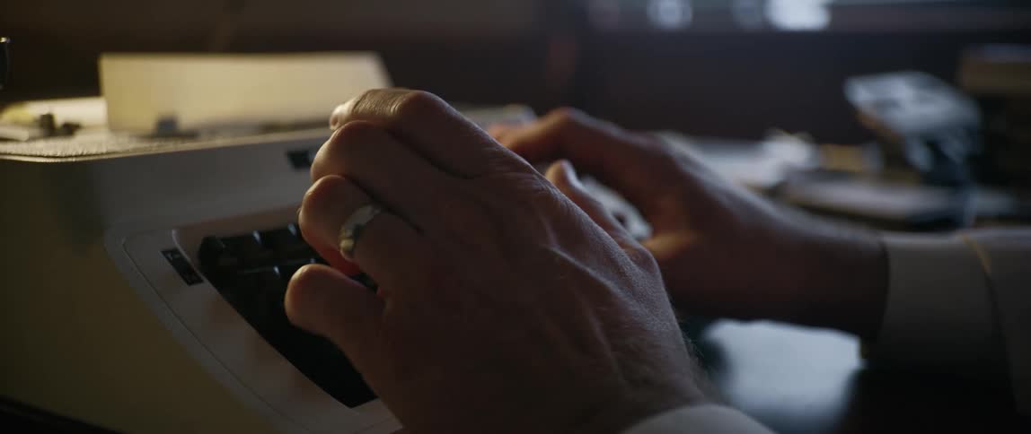 A man types at the typewriter at his desk