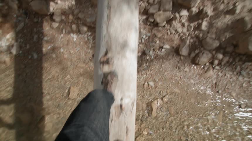 Person walking on a log over a rocky stream