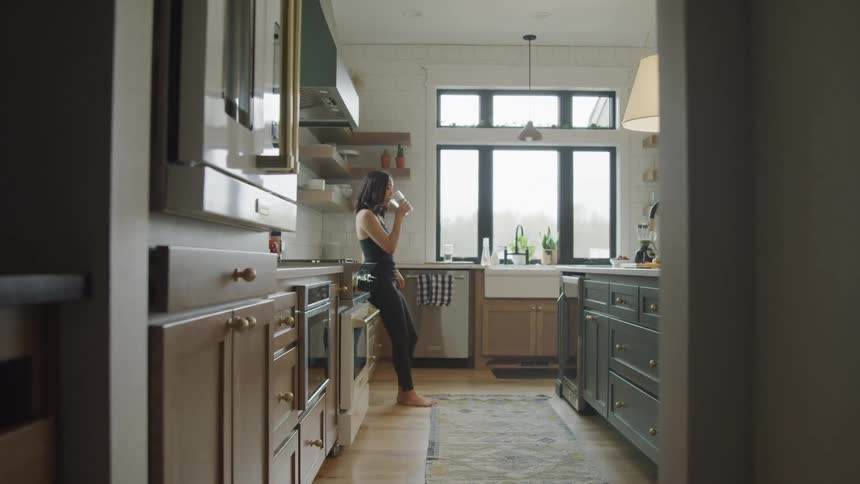 Woman in the kitchen drinking from a glass container