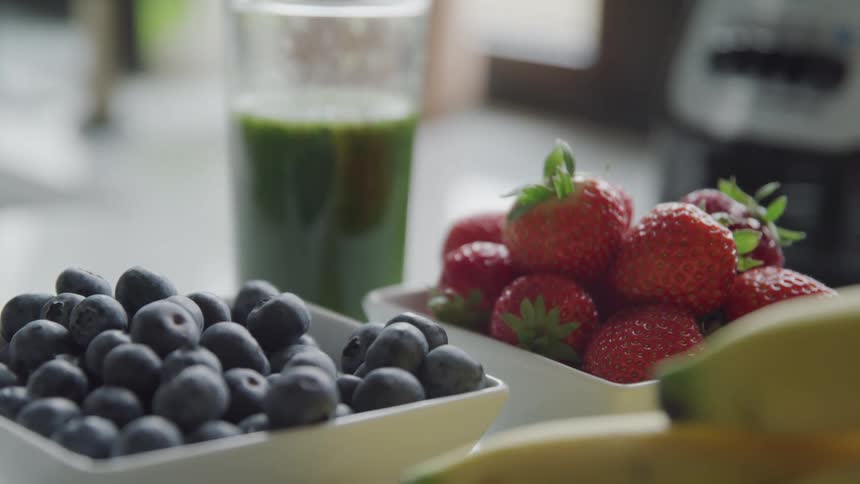 Square bowls of blueberries and strawberries displayed next to a glass of green smoothie